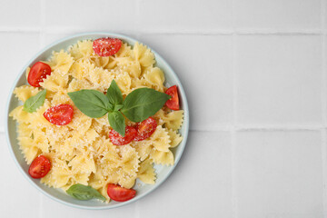 Tasty pasta with tomato, cheese and basil on white tiled table, top view. Space for text