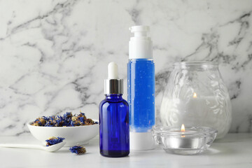 Spa composition. Bottles of cosmetic products, dry flowers and burning candles on white marble table