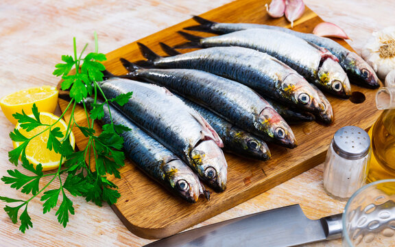 Raw sardines with lemon, parsley, garlic and spices on cutting board on wooden background