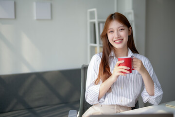 Smiling woman enjoying a cup of coffee in a bright, modern office setting, wearing a white striped shirt.