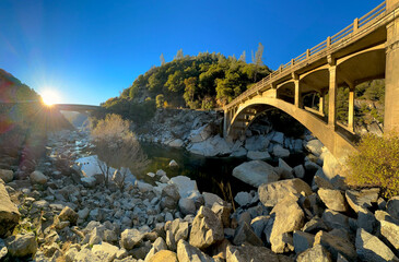 Panoramic view of the old and modern Route 49 arch bridge. Sun being the mountain and highway. Low river water level with rocky surface. South Yuba River State Park, Nevada County, California USA. - Powered by Adobe