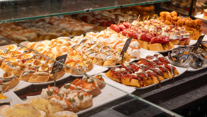 Typical snacks of Basque Country, variety of pinchos or pinxtos oven baked sea food, bread, skewers with jamon, goat cheese served in bar in San-Sebastian or Bilbao, Spain, close up