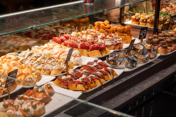 Typical snacks of Basque Country, variety of pinchos or pinxtos oven baked sea food, bread, skewers with jamon, goat cheese served in bar in San-Sebastian or Bilbao, Spain, close up