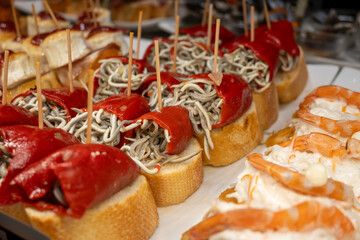 Typical snacks of Basque Country, variety of pinchos or pinxtos oven baked sea food, bread, anchovy, shrimps salad, cheese served in bar in San-Sebastian or Bilbao, Spain