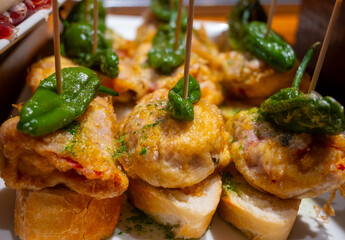 Typical snack of Basque Country, pinchos or pinxtos skewers with small pieces of bread, fish, sea food, sweet green pepper served in bar in San-Sebastian or Bilbao, Spain, close up