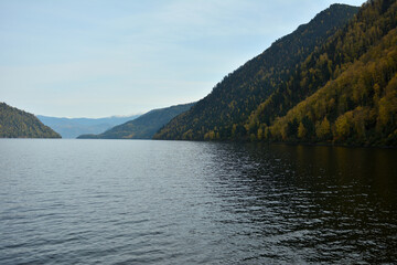 A look at the surface of a large lake surrounded by steep mountain slopes covered with dense coniferous forest on a sunny autumn day.