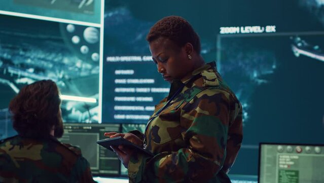 Woman high tech specialist studying satellite CCTV visualization on a big screen, preparing troops with insight for a new national safety mission. Female first lieutenant in command post. Camera A.