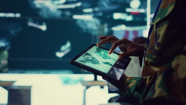 Army soldier reviews targets on a satellite world map to ensure global protection, works on tablet in military command center. Private examines battlefield data for intelligence. Close up. Camera B.