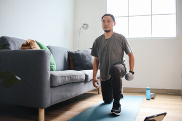 Asian sporty man doing exercise with dumbbell on yoga mat at home
