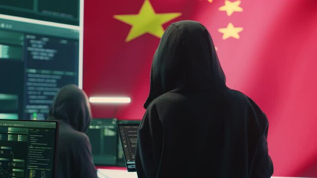 Chinese hacker working in governmental hacking room with Chinese flag on a big screen. Having the mission on inflicting fear and misinformation among the population. Dictatorship propaganda. Camera A.