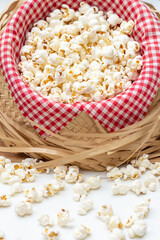 Front view of a tilted straw hat with red and white checkered fabric and salted popcorn inside. With loose popcorn scattered in front. Typical food for the São João June festival.