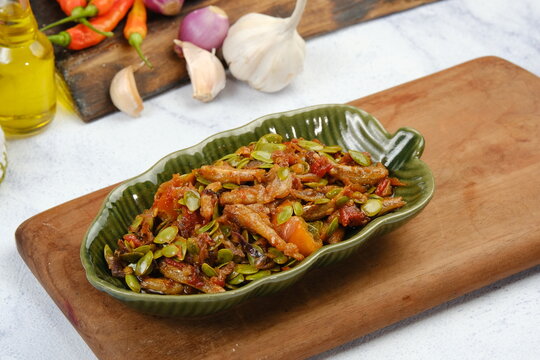 A flavorful sambal petai cina or lamtorodish placed on a wooden board with raw garlic, chilies, and spices surrounding it.