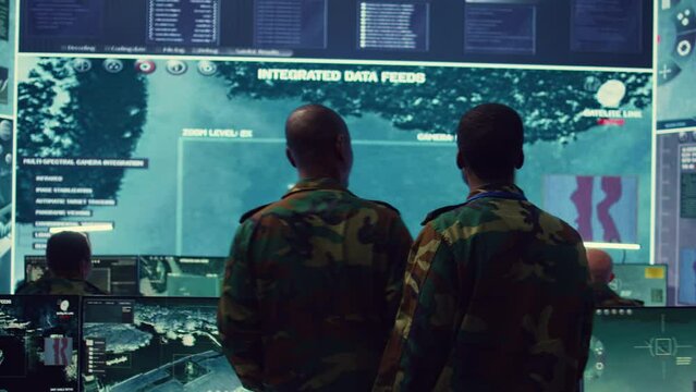 High ranking military personnel briefs the crew for a new federal mission, showing CCTV footage of satellite radar target ships for reconnaissance. Army officers provide intelligence. Camera B.