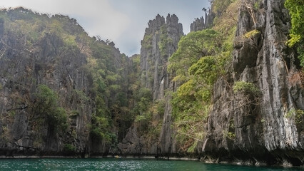 Picturesque karst rocks surround the emerald lagoon. There is green tropical vegetation on the steep furrowed slopes. Philippines. Palawan. El Nido. Small lagoon. Miniloc island. Bacuit Bay. 