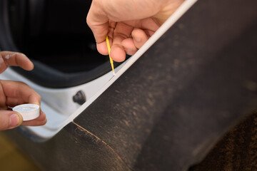A man repaints a scratch on a car part in an auto repair shop with precision and craftsmanship