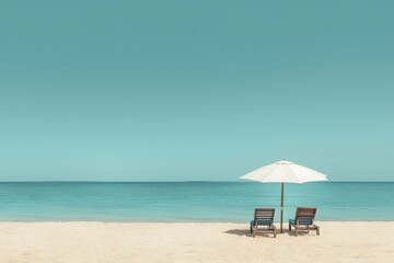 Two lounge chairs under a white umbrella on a serene sandy beach with a clear blue sky and calm ocean waters in the background.