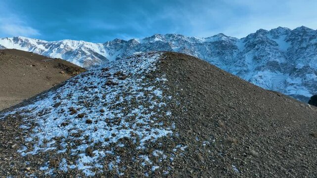 Drone flies slowly upwards at a mountain peak in Skardu and a mountain range with snow appears in the background