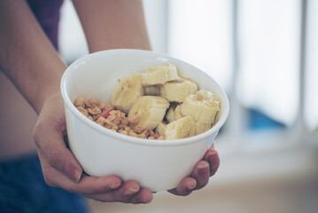 Asian women eating cereal oatmeal with milk organic nutrition ingredients. Women hands holding spoon and bowl with healthy dairy product cereal, fruits, banana. Dietary healthy lifestyle at home