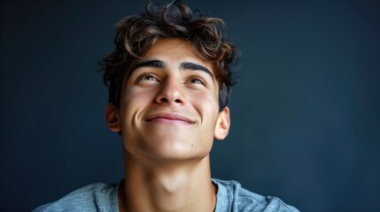 Portrait of a Smiling Young Latin Man Looking Upward with Dark Wavy Hair on Dark Blue Background