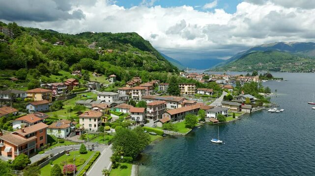 Aerial View Of A Picturesque Waterfront Town With Colorful Buildings Bordering Pella Lake, Backed By Green Hills On Sunny Day. Push Forward Shot