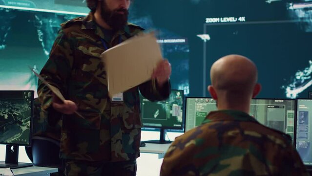 Staff sergeant providing mission files to brief his operational crew, working on gathering intelligence from surveillance systems. Prepares for various combat scenarios and outcomes. Camera A.