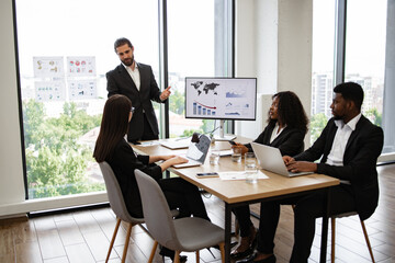 Businessman reports to colleagues standing near graphs and charts on monitor, screen, display....