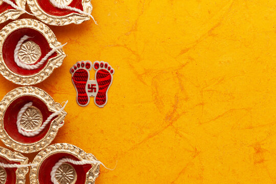 Top view of decorative Diwali Diyas (Earthen oil lamps) with Indian Hindu religious Goddess Laxmi "Charan Paduka" (written in Hindi), on an orange background.