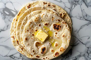 Stack of freshly cooked roti with butter on a marble surface