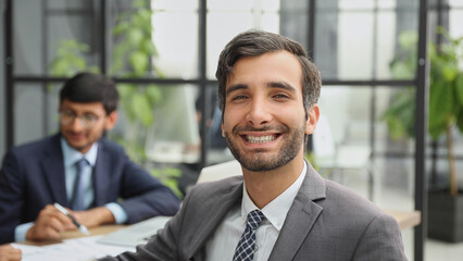 male boss against the background of her colleagues looks at the camera in a modern office