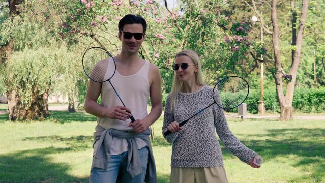 outdoors in a park with trees young brunette guy stands next to a blonde girl bambinton rackets best friends relaxing together