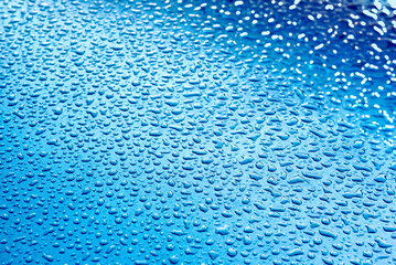 Wassertropfen auf einer grau-blauen Oberfläche mit leichtem Schärfe- und Farbverlauf und leichtem Bokeh am rechten Rand