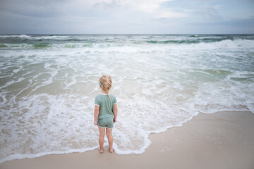 Young child standing on shore watching ocean waves