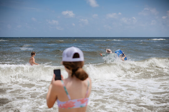 Girl taking a phone video of her family playing in beach waves