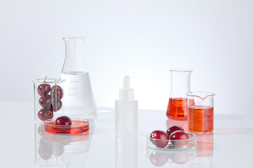 Cosmetic advertising mockup on white background, decorated with fresh cherry and lab items. Red and transparent liquid filled in glassware, blank label cosmetic bottle displayed in center