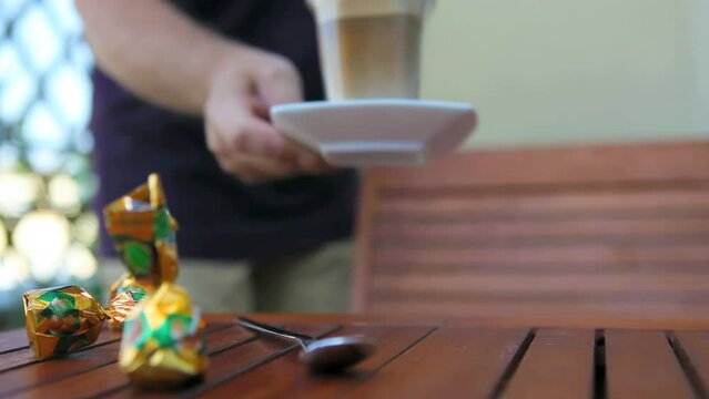 Male hand puts a glas with caffee late macchiato on a table 