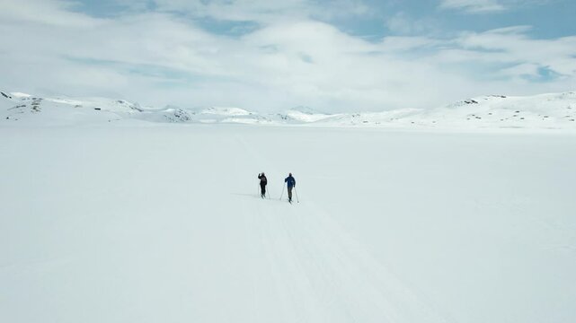 Two people are cross country skiing across a snowy landscape on a frozen lake in Tyin, Norway.