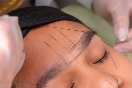Using pre-inked mapping string to make guide lines around the eyebrows for approximate shaping for microblading procedure.