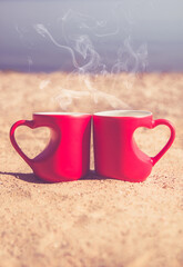 two heart shaped mugs with tea on the seashore
