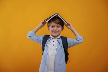 Book is above the head, having fun. Little boy is in the studio against yellow background