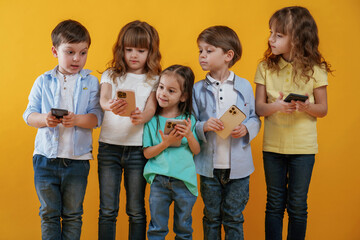 Obraz premium Using smartphones. Kids are together against yellow background