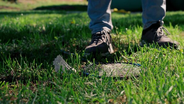 on the street in the park on the green mown grass lies a white shuttlecock for playing bambinton an element of sports boy lifts the shuttlecock