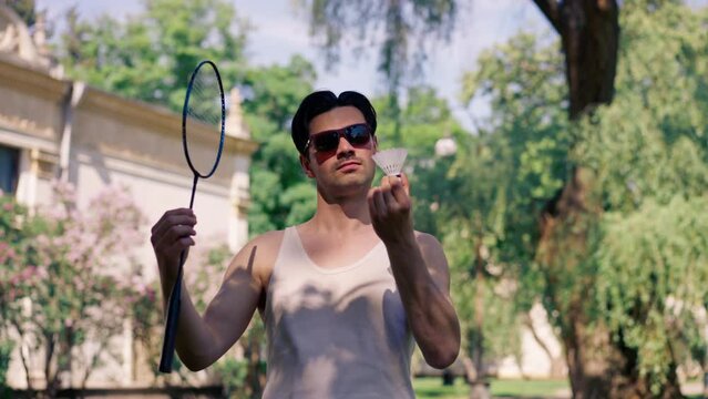 outdoors in a park with trees young brunette boy standing with a bambinton racket trying to tighten the strings on the racket ready to play
