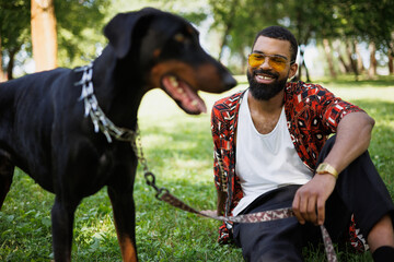 Smiling african american man holding leash of blurred doberman dog in park