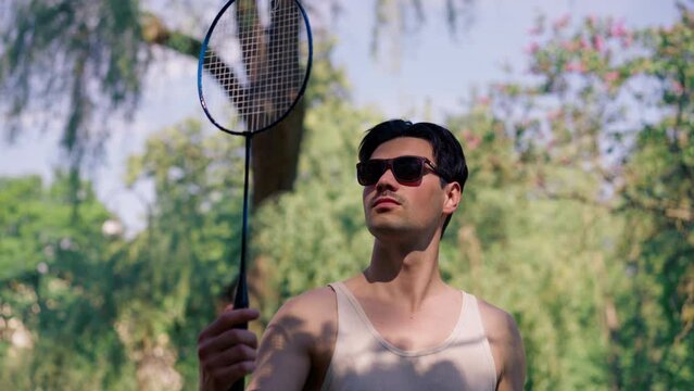 outdoors in a park with trees young brunette boy standing with a bambinton racket trying to tighten the strings on the racket