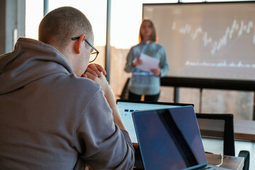 Female business trainer is against projector with business data, teaching the man