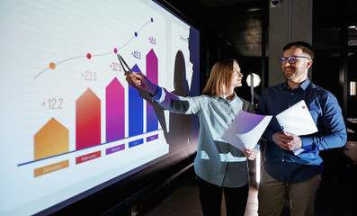 Conception of profit. Man and woman are standing near projector with business data, cooperation