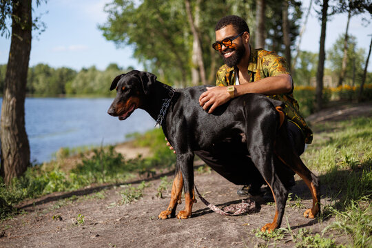 Smiling african american man hugging doberman dog near lake in park