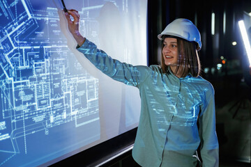 In white hard hat. Female architect is showing construction site plan for building on projector