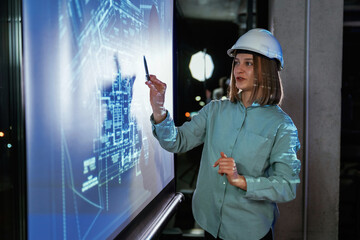 In white hard hat. Female architect is showing construction site plan for building on projector