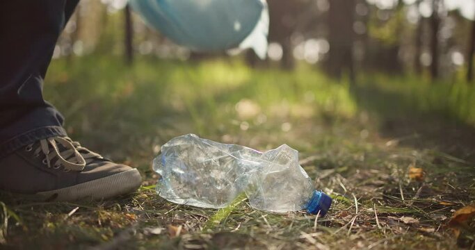 Man picking up trash plastic bottle lying on the ground in the forest